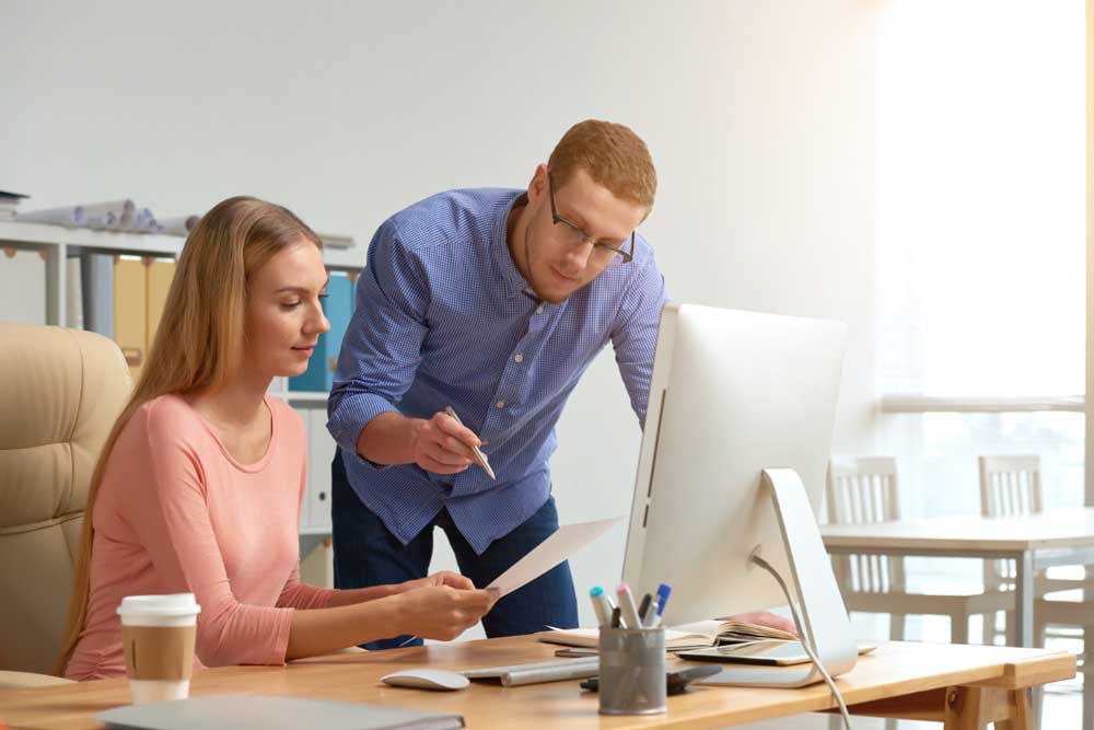 Man and woman collaborating on a business document, brainstorming ideas together in a professional office setting.