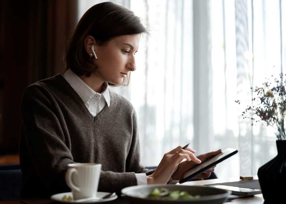 Side view of a woman holding a device, focused on the screen in a relaxed or professional setting